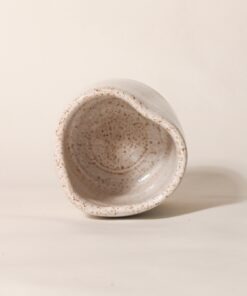 Copo Coração de cerâmica, deitado com a base em argila natural e topo em esmalte branco salpicado, em fundo neutro Esmo