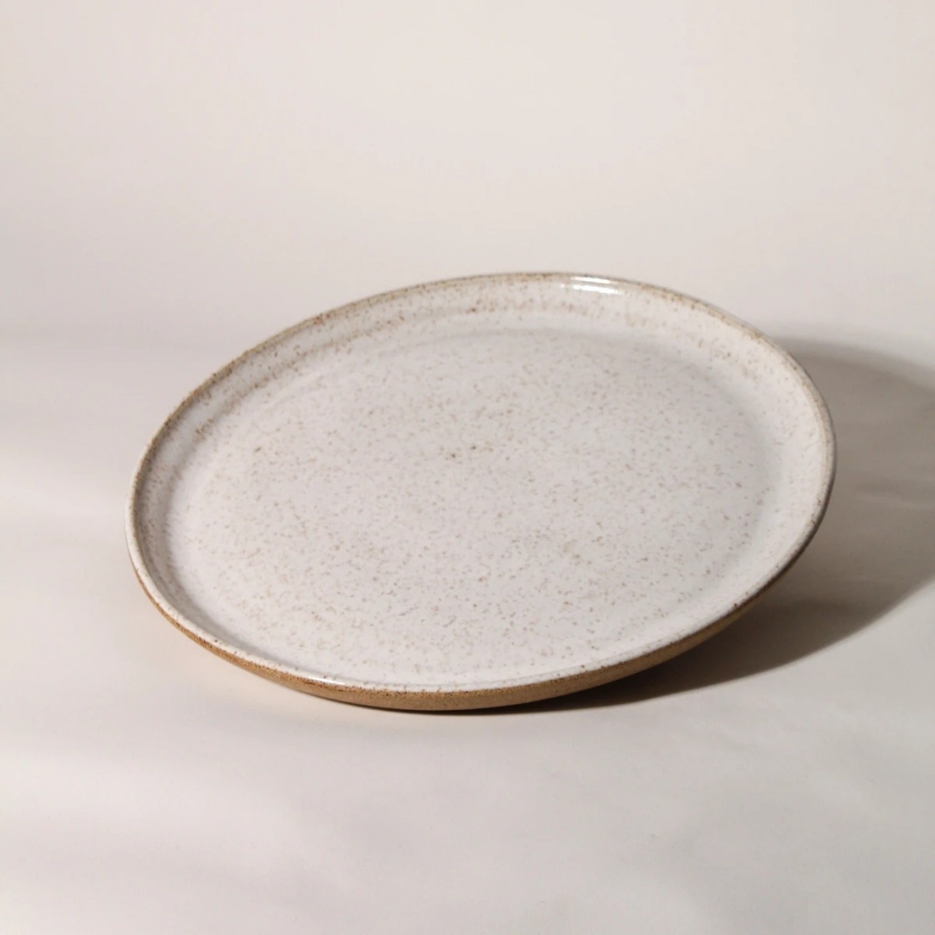 Prato de cerâmica esmaltada branco salpicado com borda em argila tabaco natural e silhueta plana. By Esmo.