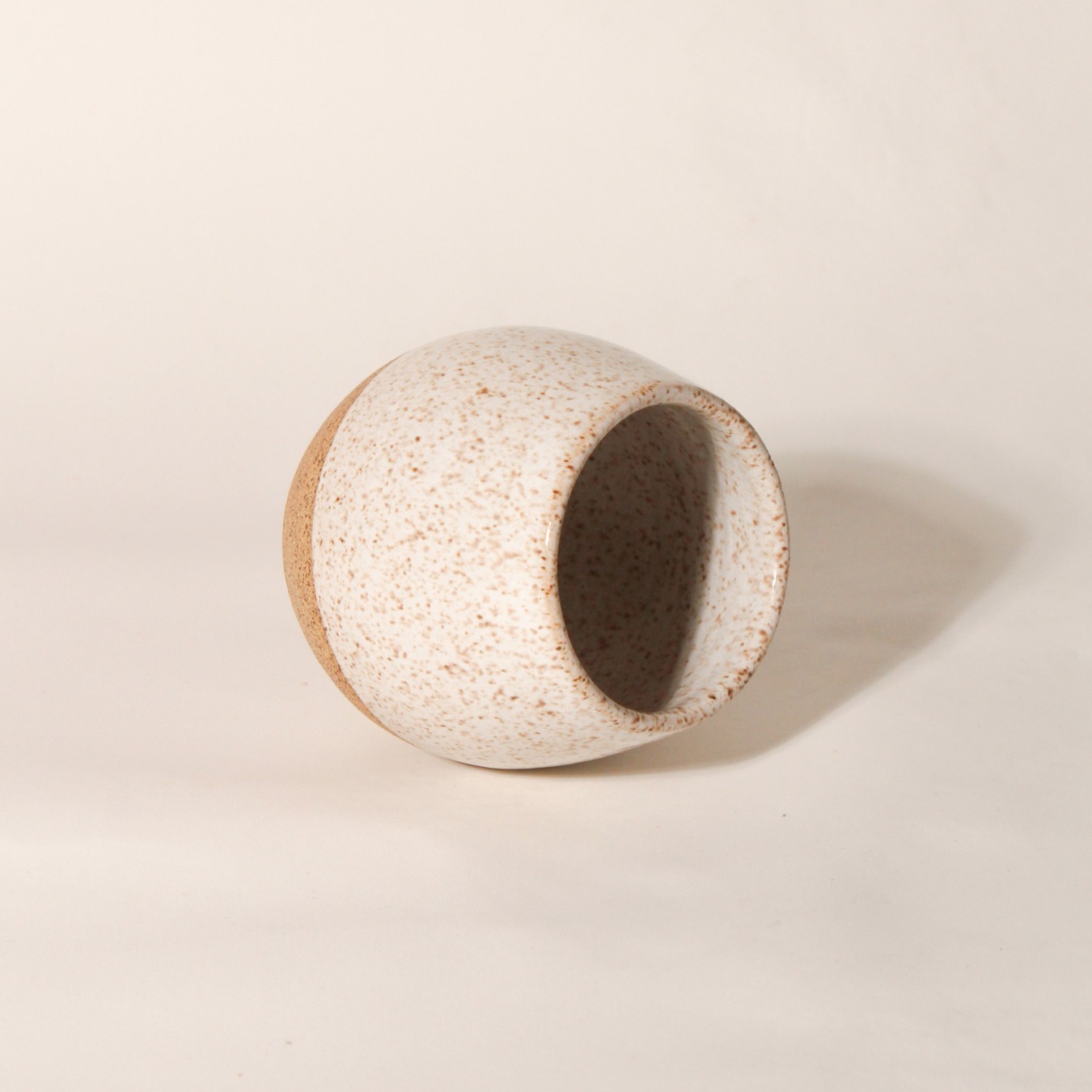 Copo Esmo de cerâmica com design autoral e acabamento em dois tons, argila natural e esmalte branco salpicado, na horizontal.